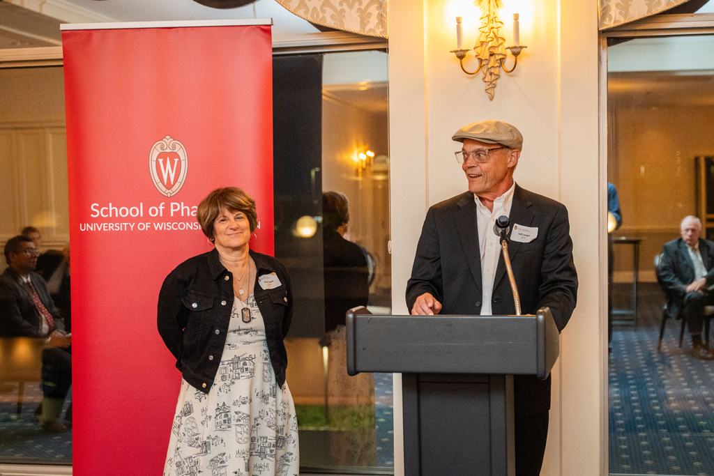 Jeff Langer speaks into a podium microphone while Patti Langer looks on