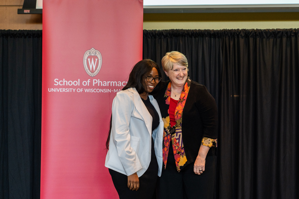 A student poses with Karen Kopacek in front of the red School of Pharmacy banner