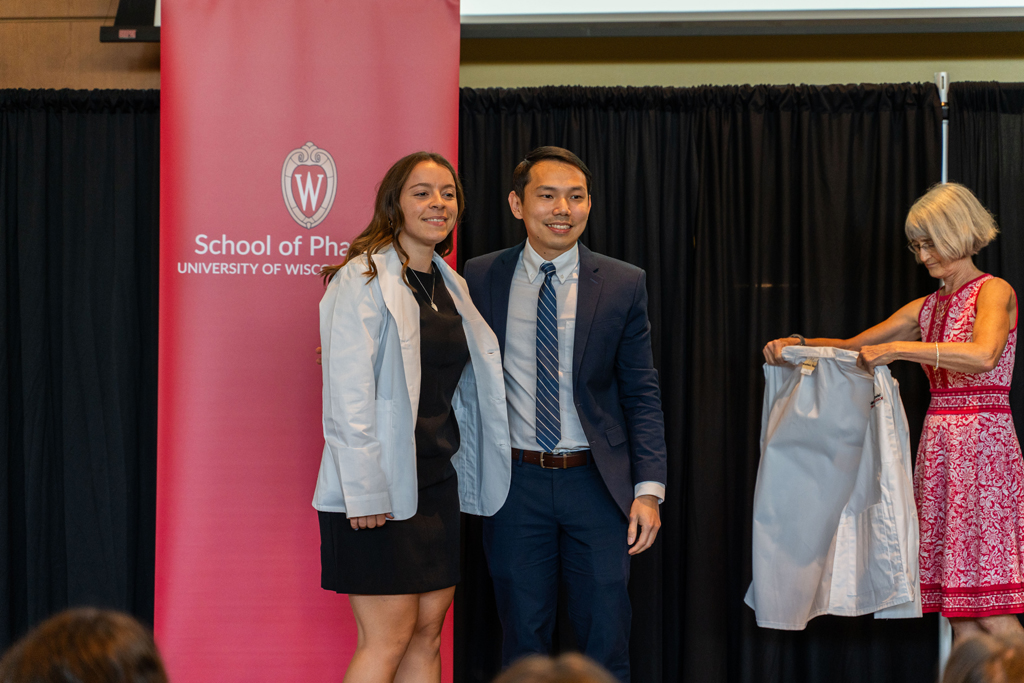 A student poses with Sean Lim in front of the red School of Pharmacy banner