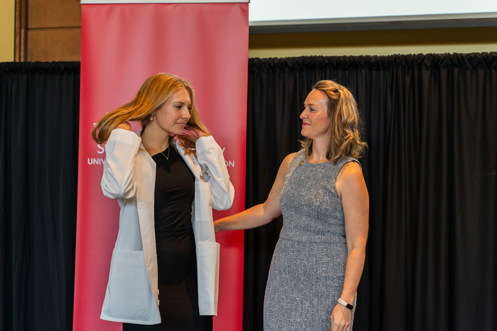 A female student adjusts her hair after receiving her white coat from Kate Rotzenberg