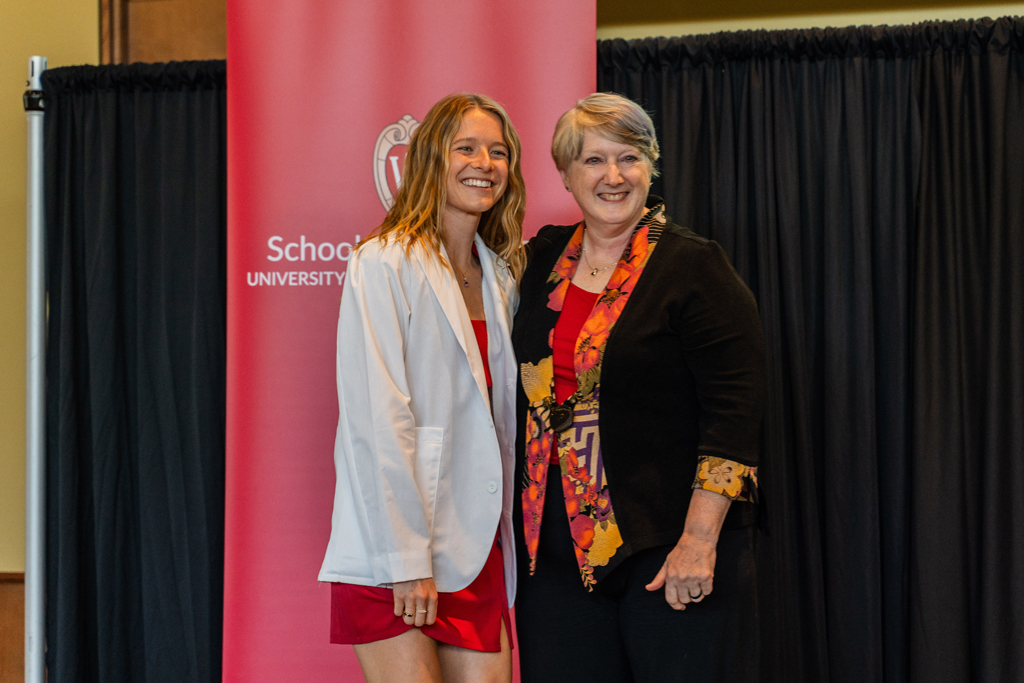 A student poses with Karen Kopacek in front of a red School of Pharmacy banner