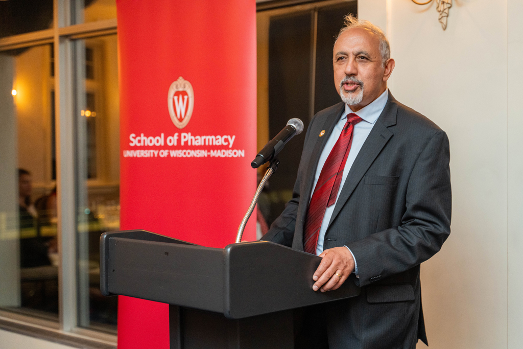 Harry Sharata speaks at a microphone in front of a red School of Pharmacy banner