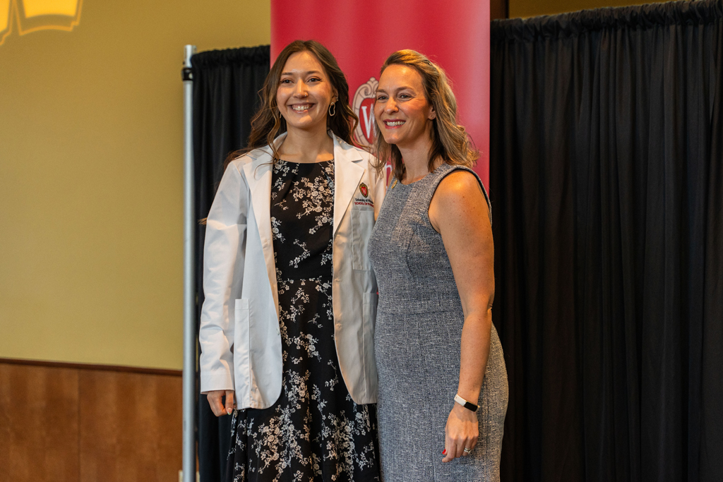 A student poses with Kate Rotzenberg in front of a red School of Pharmacy background