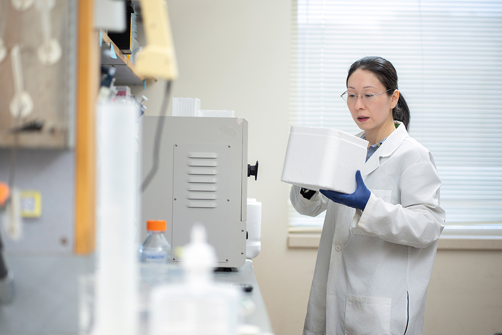 Jiaoyang Jiang in a white coat carrying a piece of white equipment in a lab