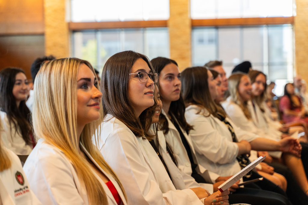 Students in white coats smile and listen to a speaker