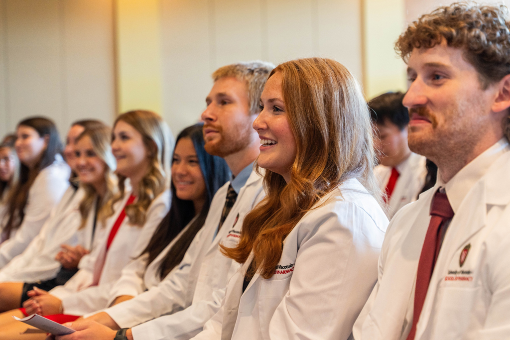 Students in white coats smile and listen to a speaker