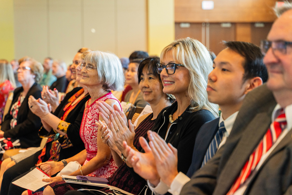 Faculty and staff — including Kate Rotzenberg, Karen Kopacek, Mara Kieser, Michelle Chui, Beth Martin, Sean Lim, and Dean Steve Swanson, applaud.