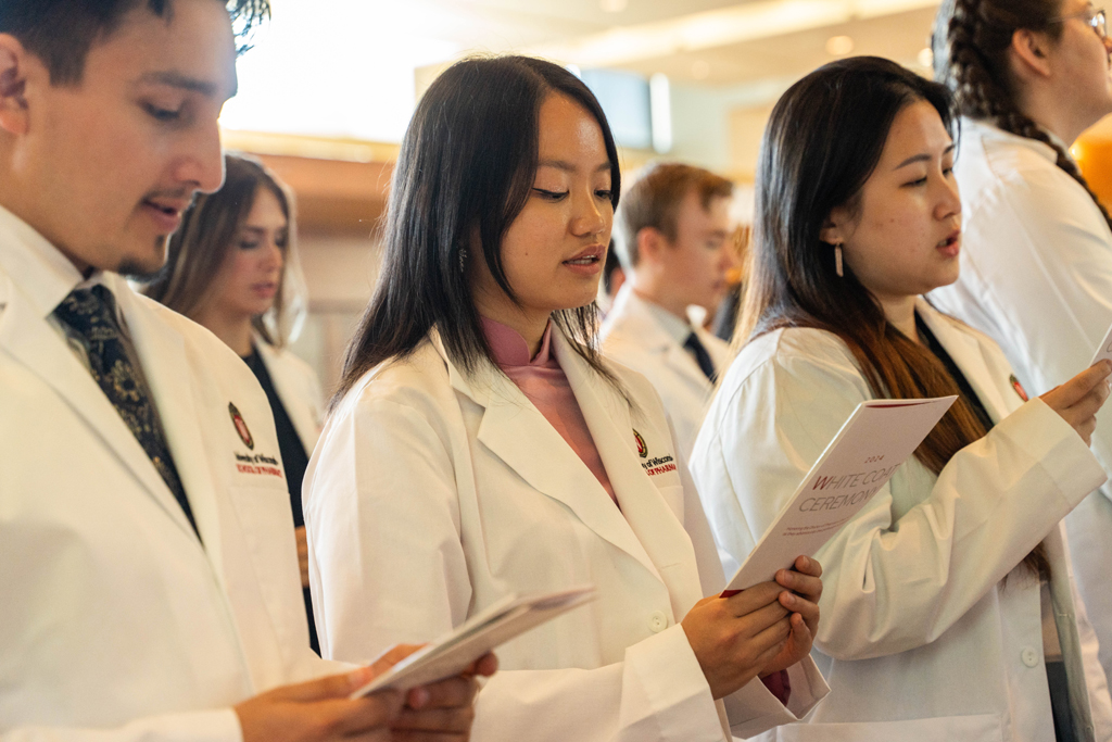 Students in white coats read the Oath of a Pharmacist off of the backs of their White Coat Ceremony programs