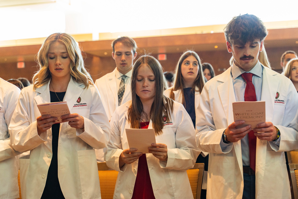 Students in white coats read the Oath of a Pharmacist off of the backs of their White Coat Ceremony programs