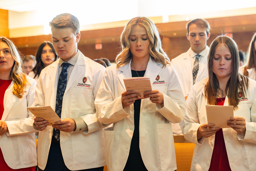 Students in white coats read the Oath of a Pharmacist off of the backs of their White Coat Ceremony programs