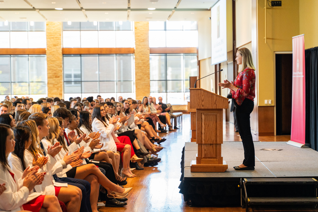 Second-year PharmD student Katie Molkentin speaks at a podium to the Class of 2028 seated in chairs