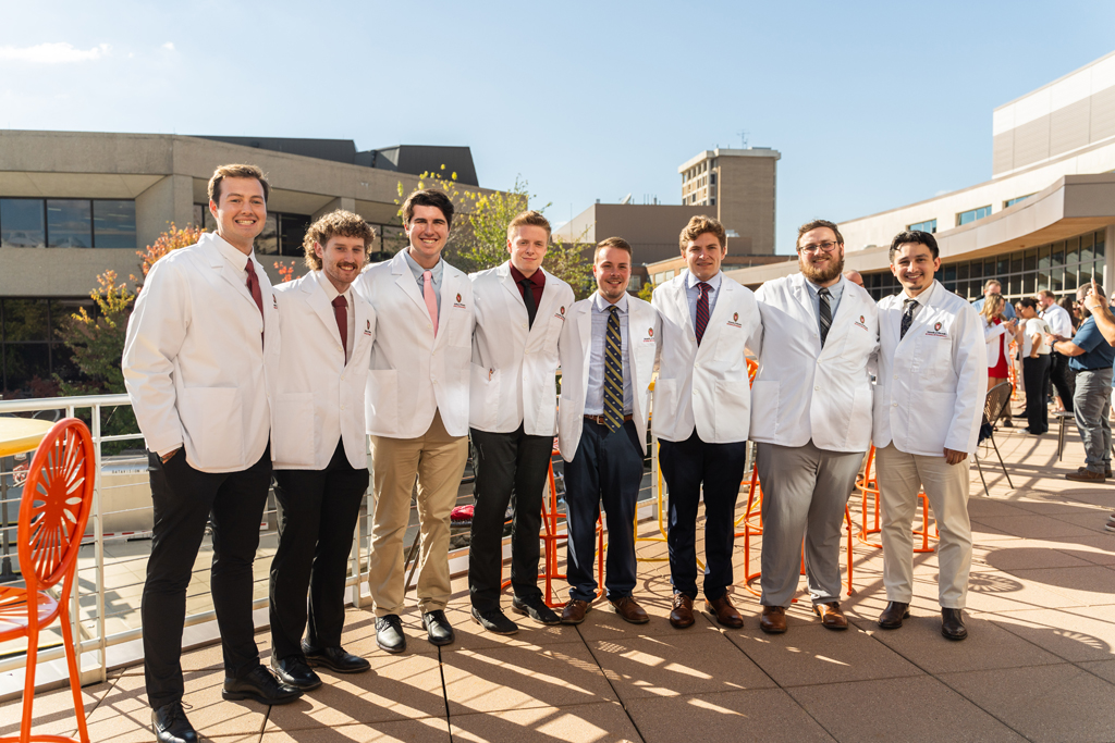 A large group of eight male students pose and smile for a photo outside