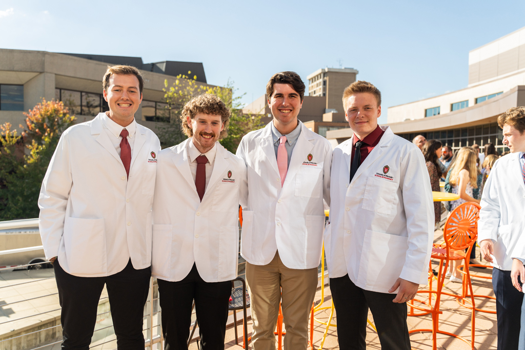 Four male students in white coats pose for a photo outside