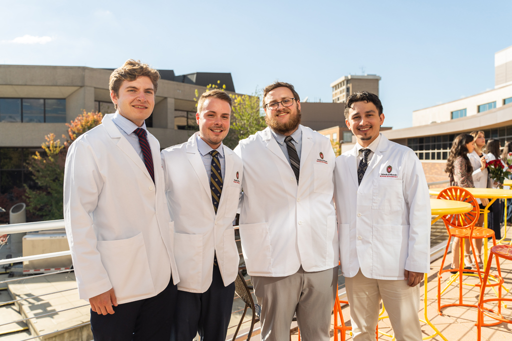 Four male students in white coats pose for a photo outside