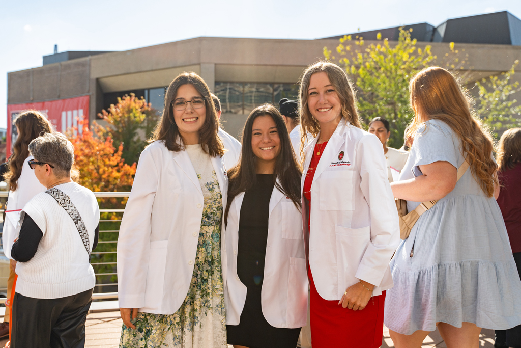 Three female students pose for a photo outside with people in the background