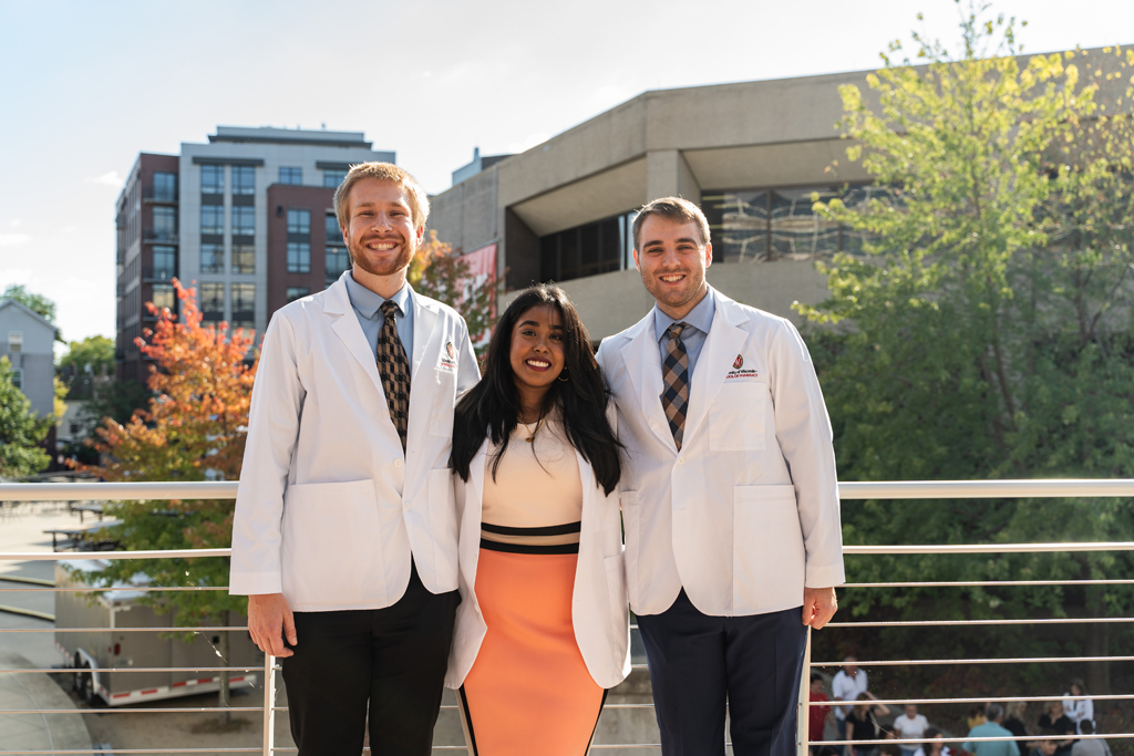 Three students in white coats pose for a photo outside