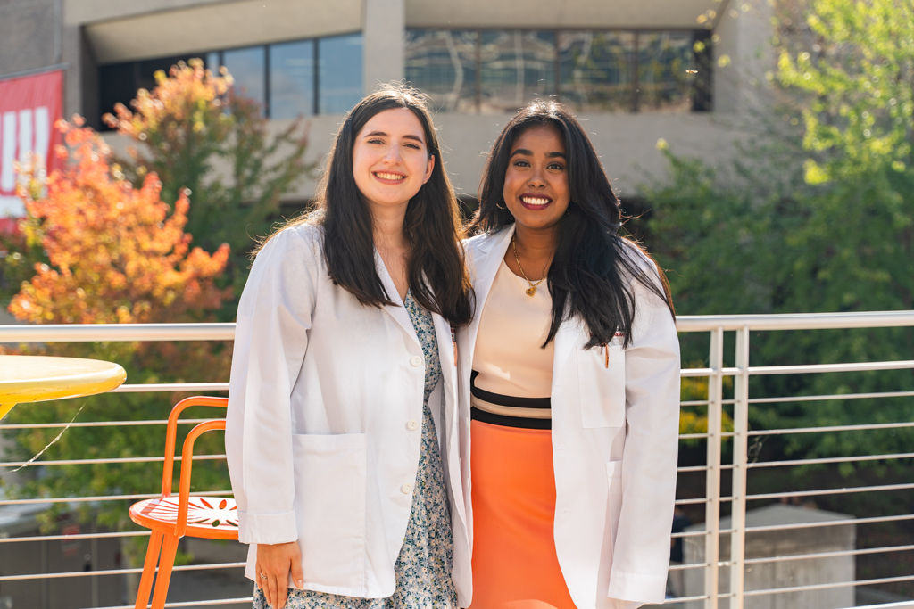 Two students in white coats smile for a photo outside