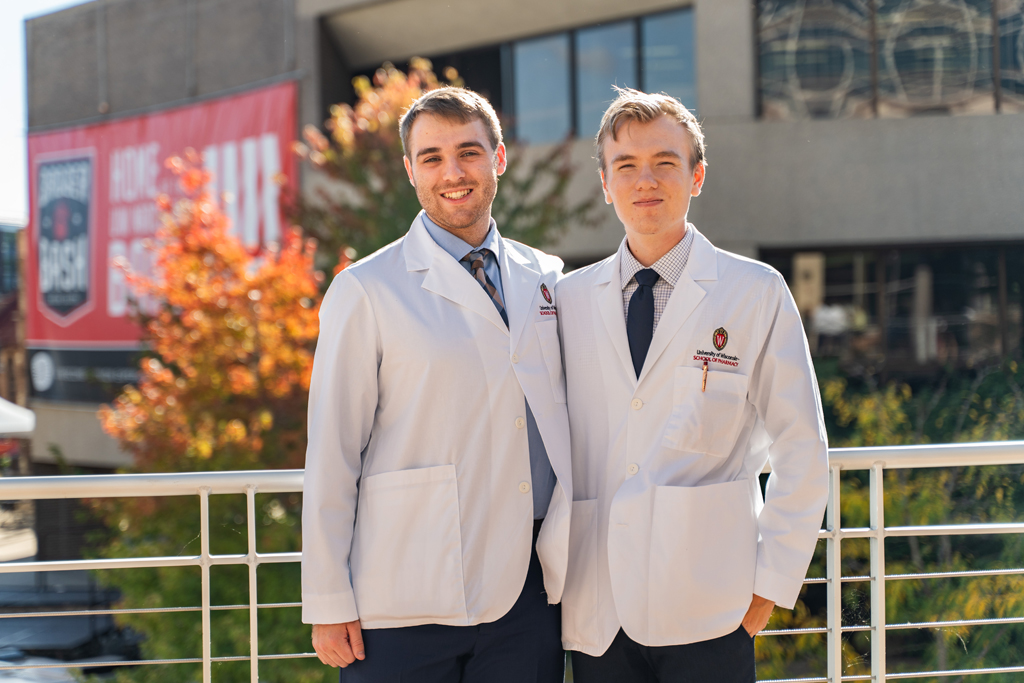 Two male students in white coats pose outside for a photo