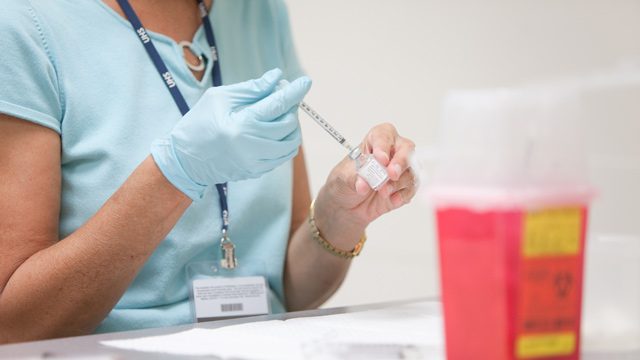 Nurse wearing glove extracting liquid from vial with syringe