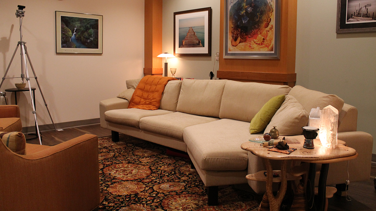 A room with a couch, a lamp, walls decorated with art, and clinical recording equipment