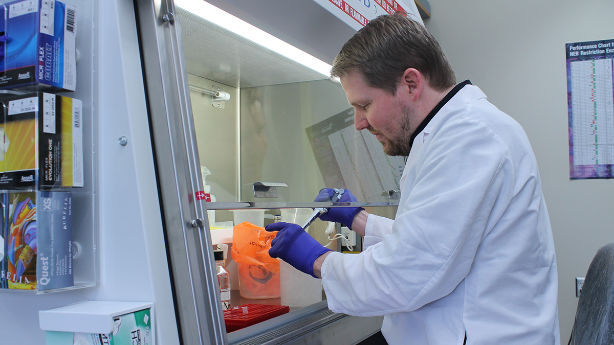 Jason Peters using a pipette under a hood in his lab