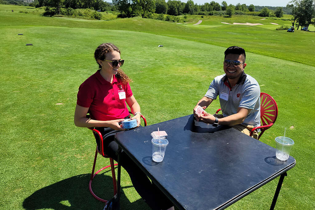 Check-in people for golfing event sitting at pop-up table in terrace chairs with tickets and cards