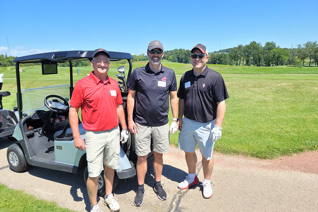 Dave Mott and other faculty in golf shirts and caps next to a golf cart