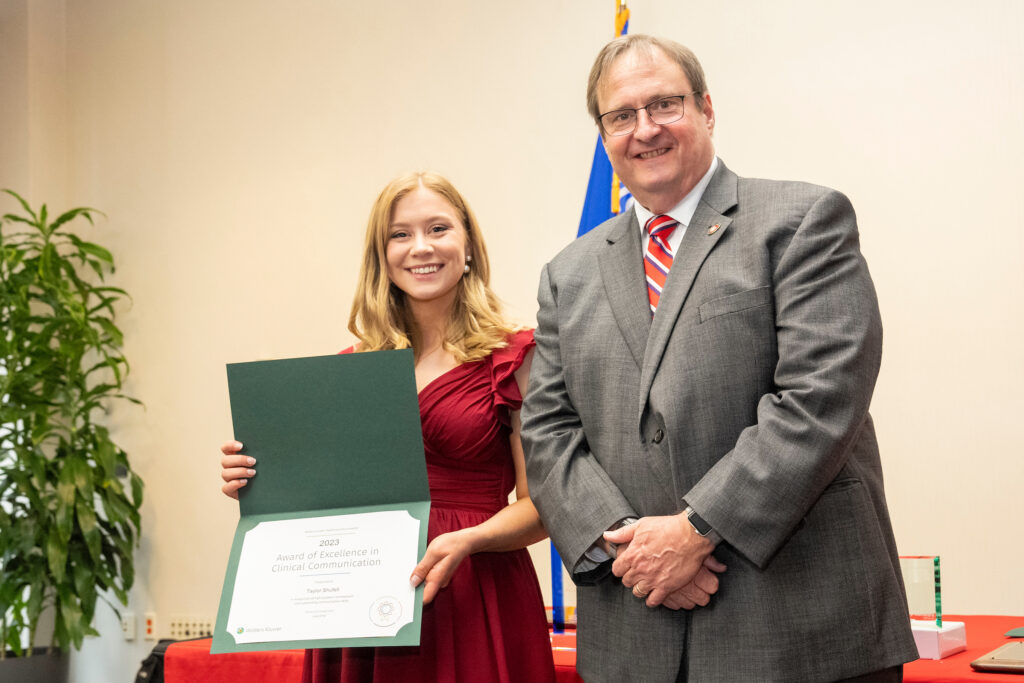 Taylor Shufelt poses with Dean Steve Swanson and the Award of Excellence in Clinical Communication.