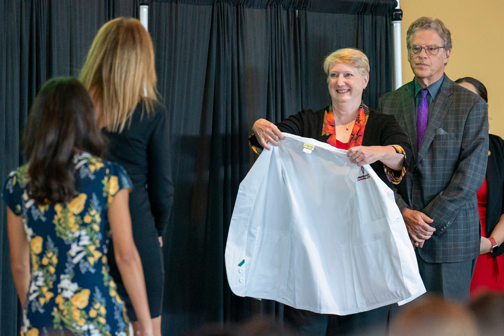 Staff offering white coat to student