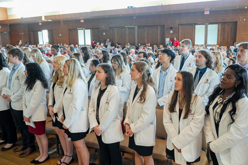 Students in white coats standing from their seats and speaking
