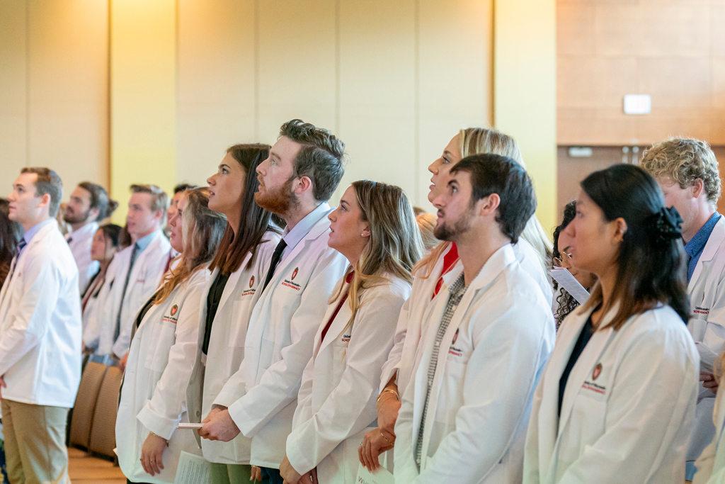 Students in white coats standing from their seats