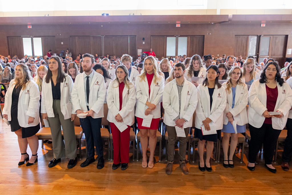 Students in white coats standing from their seats