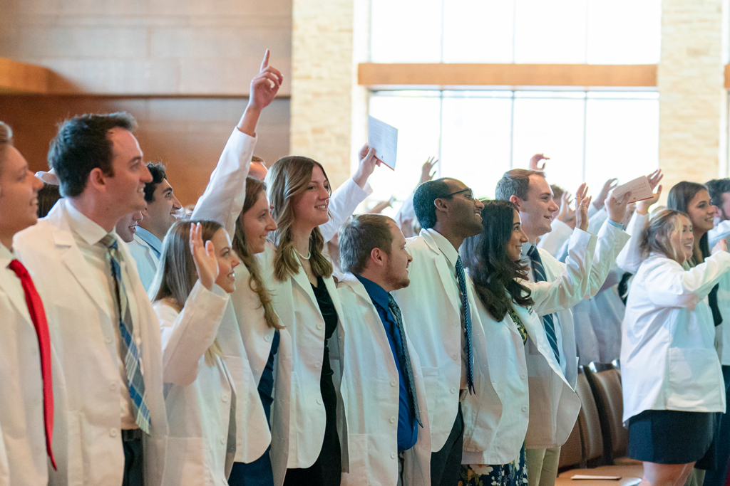 Students in their white coats celebrating in audience