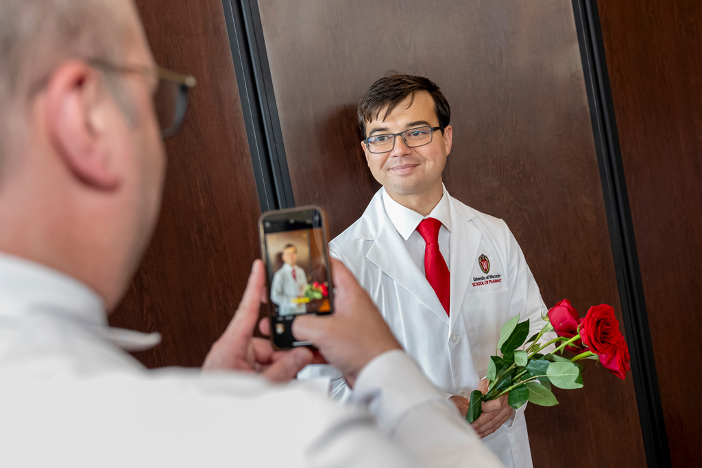A father taking a photo of his son wearing his white coat and holding roses