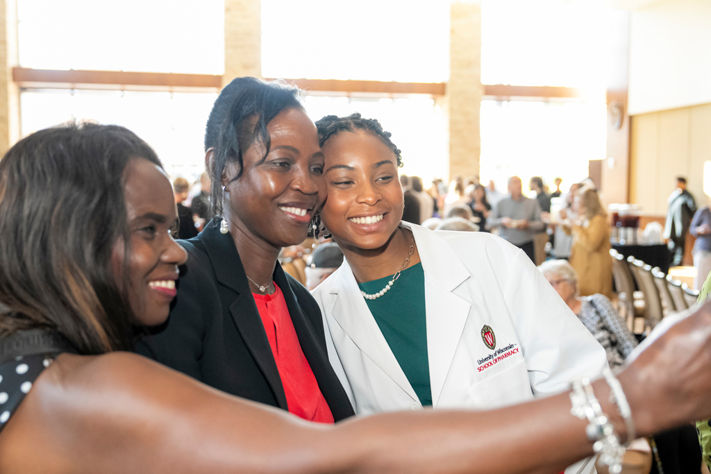 Student in white coat taking a selfie with mother and staff