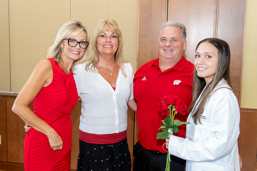 Student in white coat holding flowers together with her parents and Beth Martin