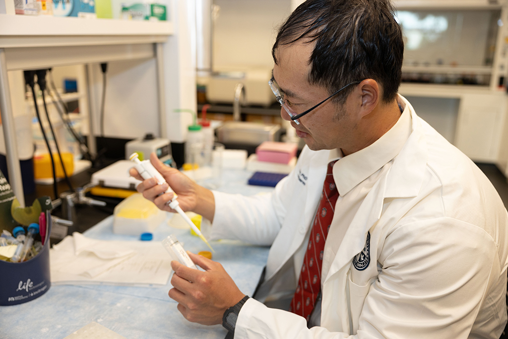 Joe Su works in his lab, holding a small white pipettor 