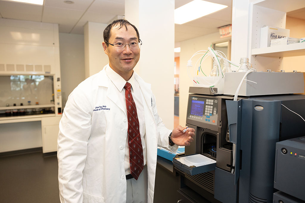 Joe Su poses next to a large grey lab machine