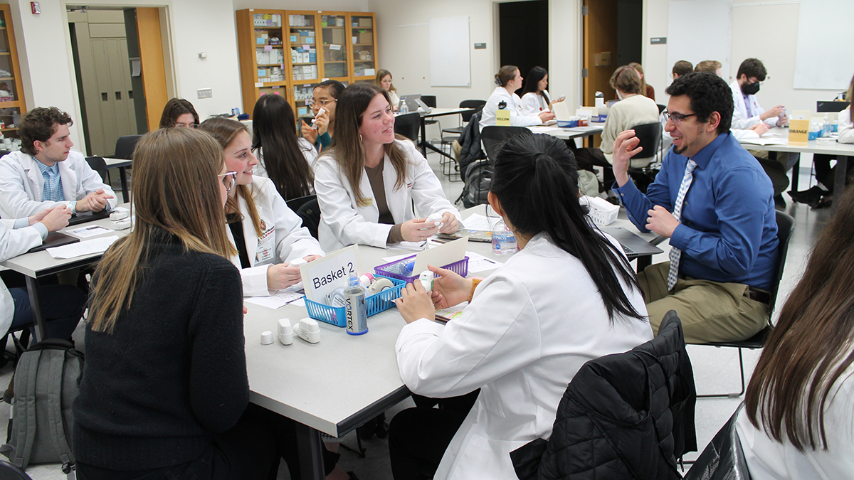 Ed Portillo speaks to a table full of students in white coats