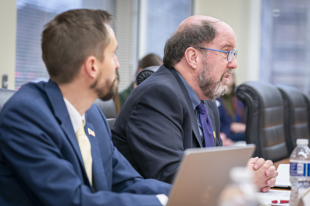 Cody Wenthur looks on as Jay Ford speaks at a conference table.