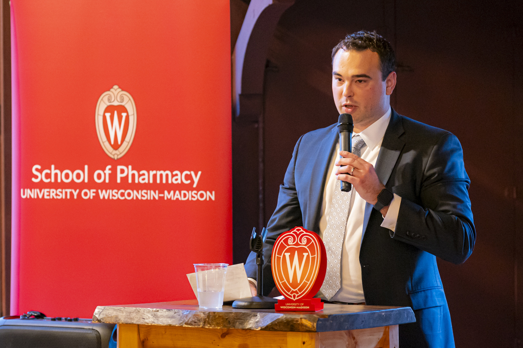 Dean Bowen speaks at a microphone in front of a School of Pharmacy banner