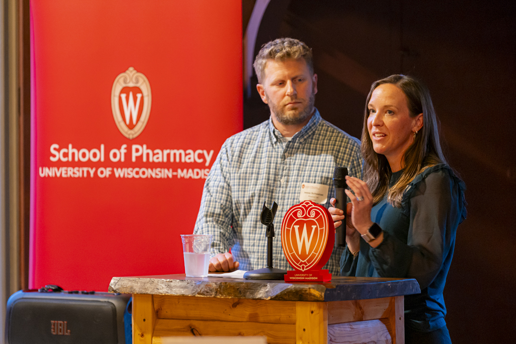 Jesse and Jessica Schaetzel speak at a microphone in front of a School of Pharmacy banner