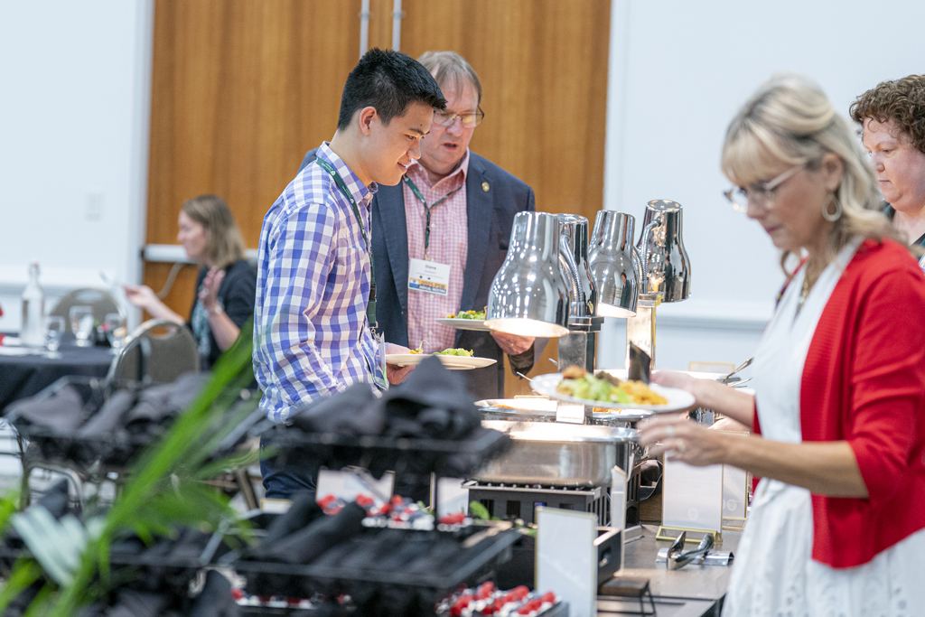 Attendees holding plates go through the buffet line