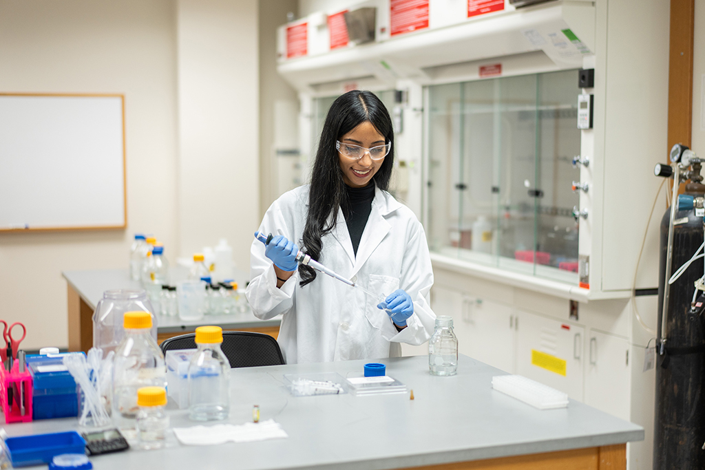 Apoorva Reddy wears a white coat and safety glasses and works in a lab