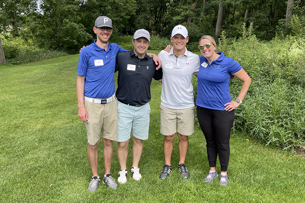 A group of alumni smile at the 2022 golf outing, outside in the sun