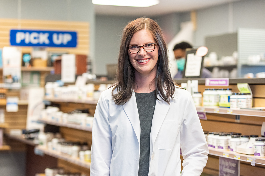 Abbi Linde in a white coat stands in a pharmacy