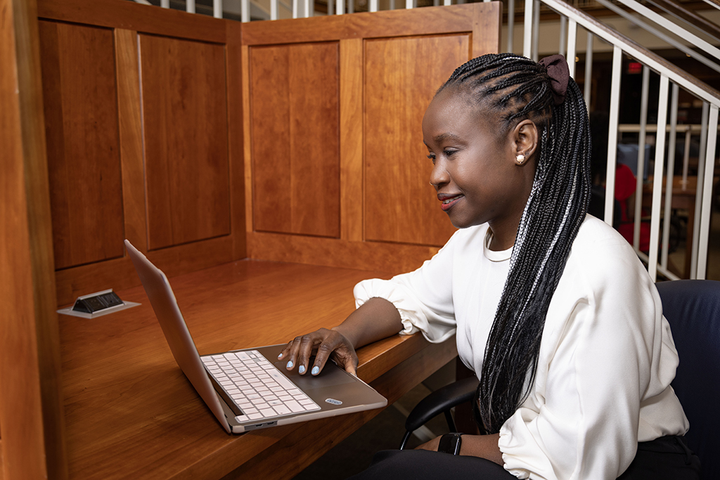 Adati Tarfa types on her computer in front of wood paneling