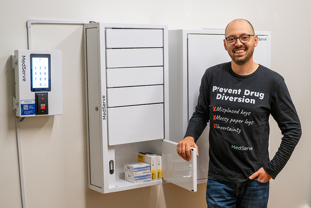 Alex Yampolsky poses next to a MedServe safe with boxes of medication inside