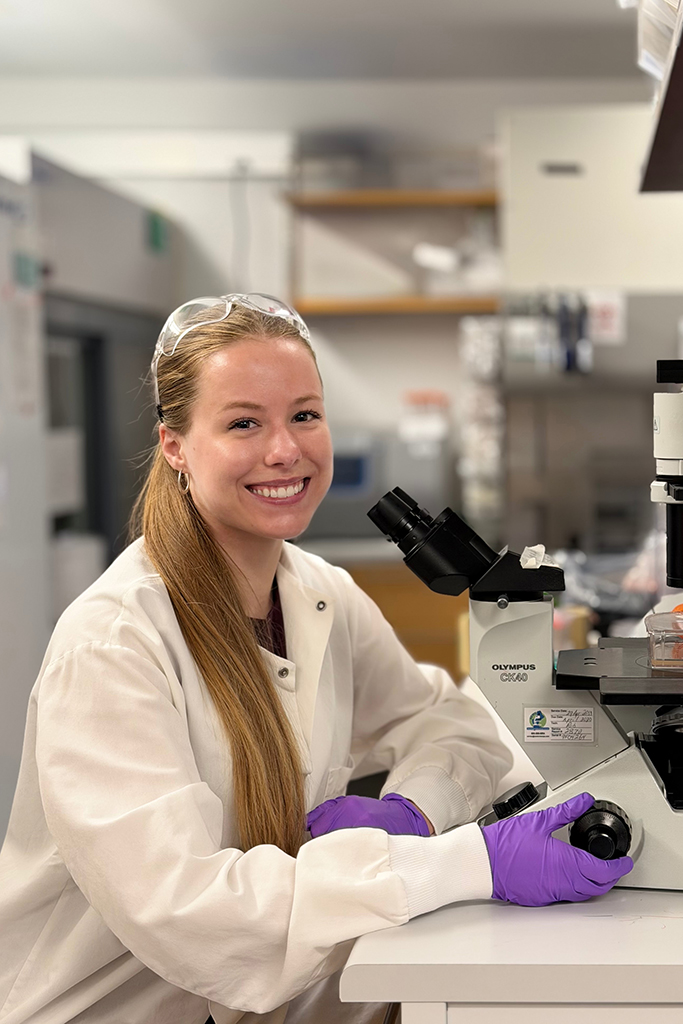 Allie Barret sitting in front of a microscope in a lab setting