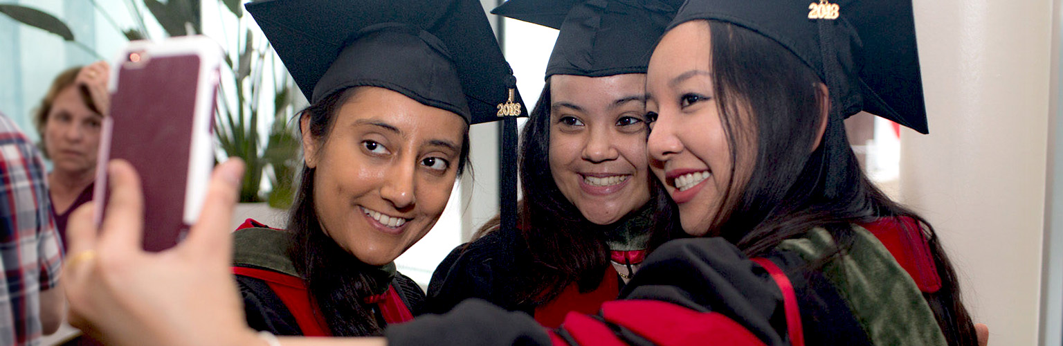 Three smiling PharmD graduates take a selfie in their graduation robes